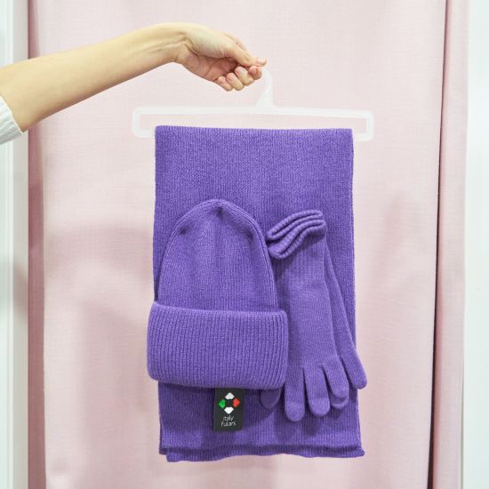 Conjunto de invierno en color lila compuesto por bufanda, gorro y guantes sostenido sobre una percha.