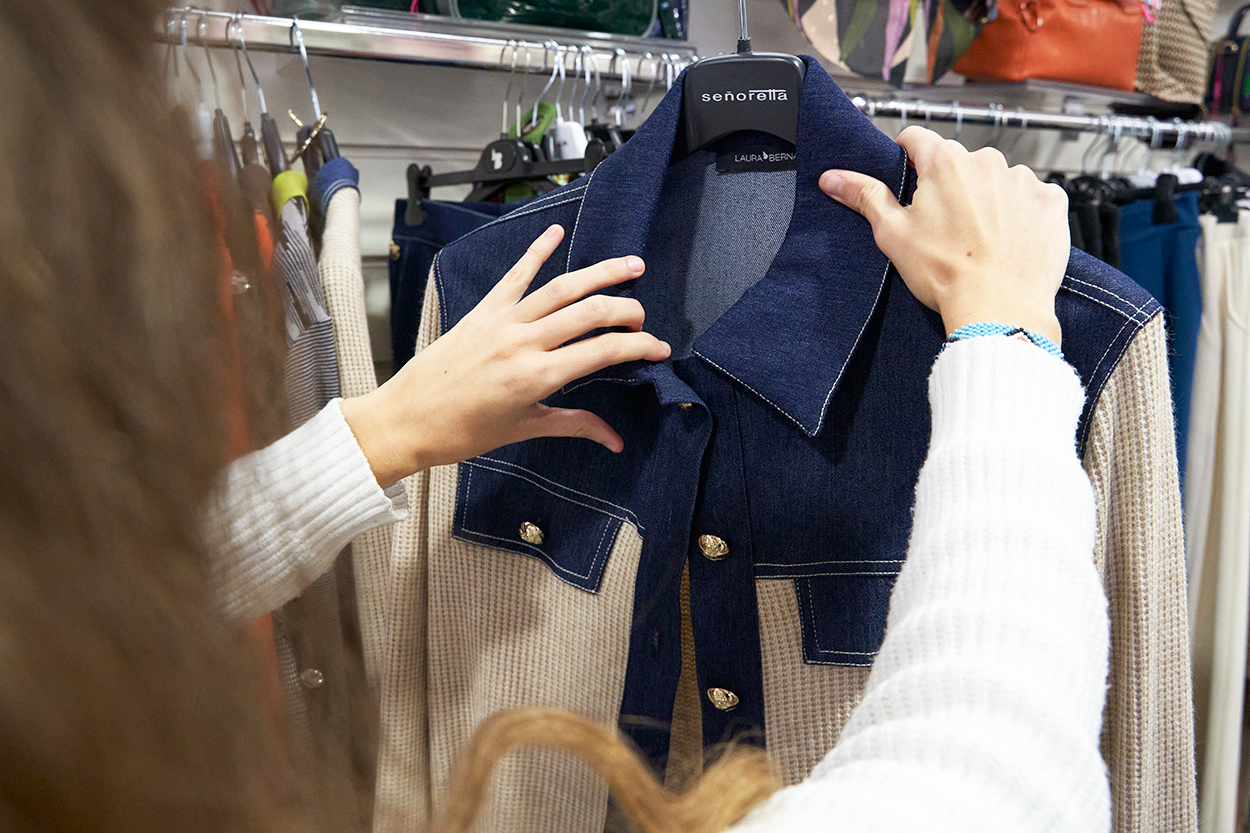 Mujer examinando una chaqueta de punto y denim en una boutique.