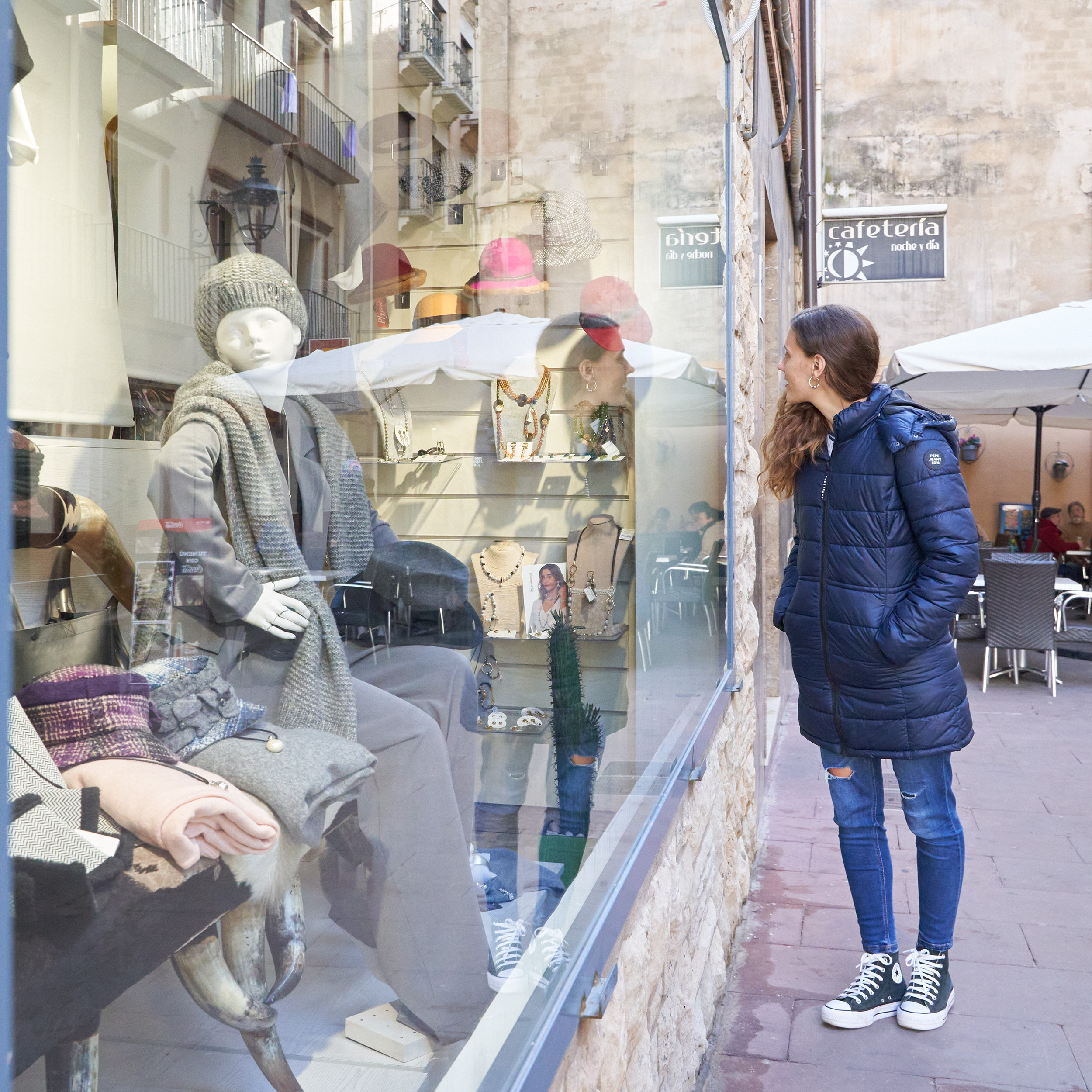 Mujer observa el escaparate de una boutique con maniquíes vestidos y bisutería en exposición.