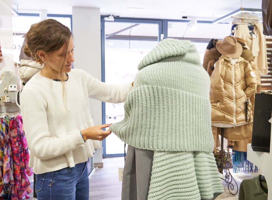 Mujer observando un conjunto de punto verde menta en un maniquí dentro de una boutique.