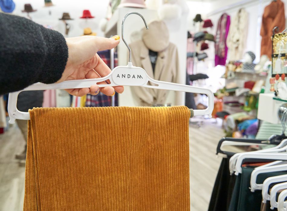 Mano sosteniendo una percha con pantalón de pana color mostaza en una tienda de ropa.