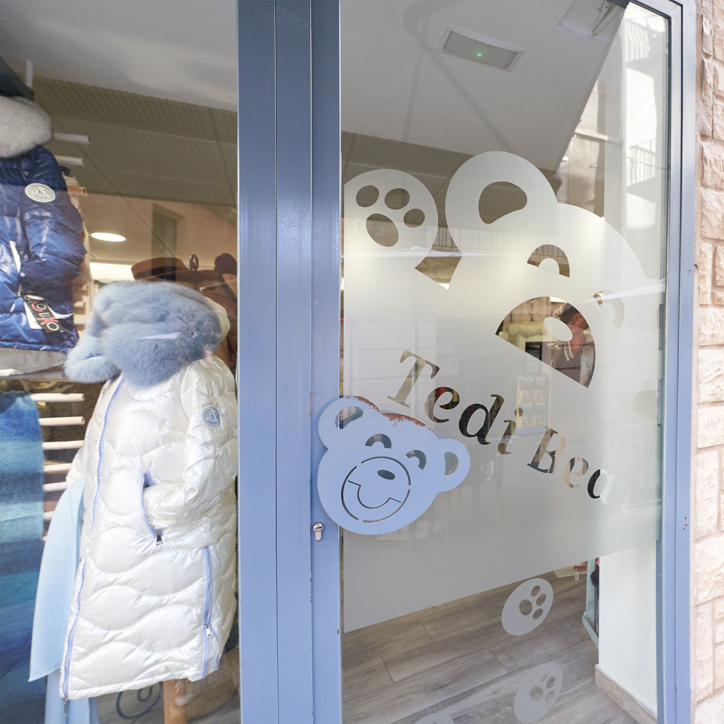 Detalle de la puerta de entrada de la tienda Tedi Bear con logotipo de oso en el cristal.
