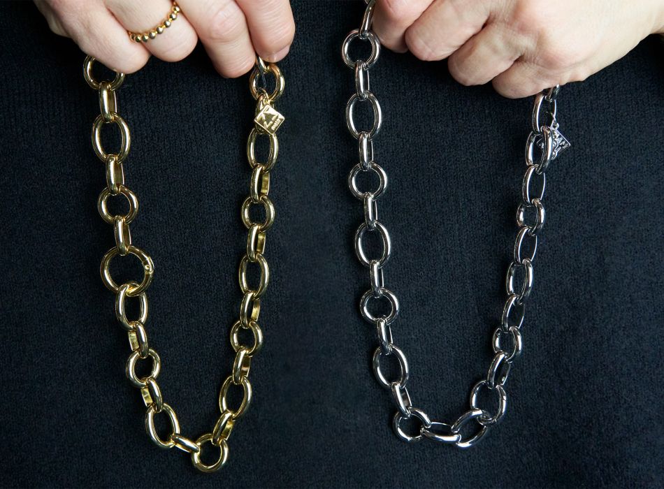 Dos collares de eslabones gruesos, uno dorado y otro plateado, sostenidos por una persona.