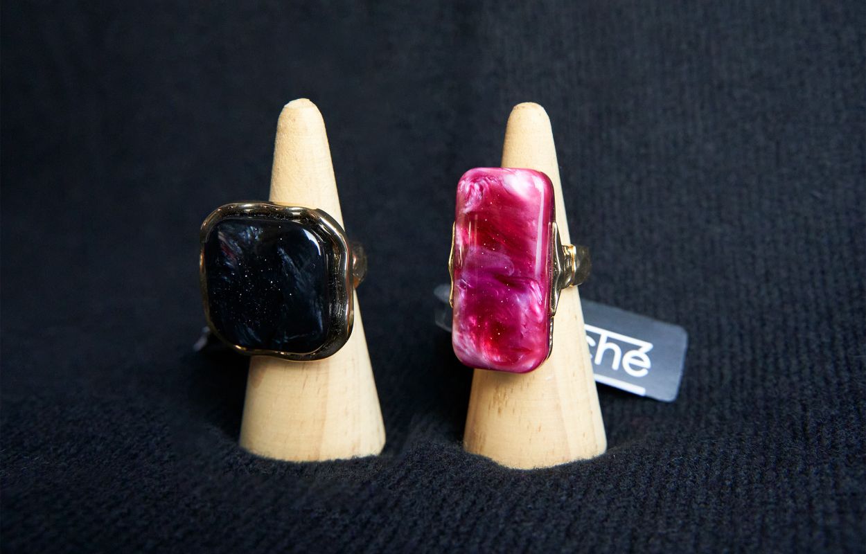 Dos anillos con piedras grandes, uno negro y otro fucsia, expuestos sobre conos de madera.
