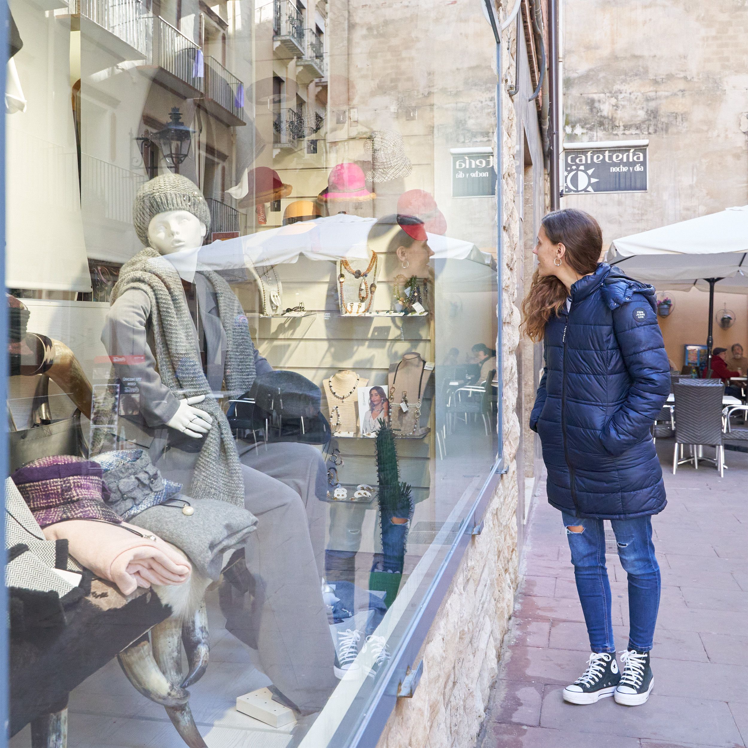 Mujer observa el escaparate de una boutique con maniquíes vestidos y bisutería en exposición.